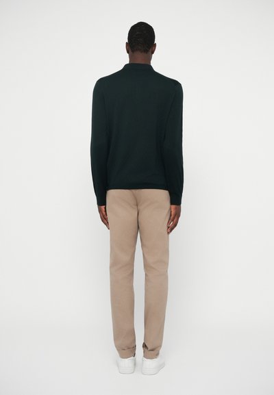 Σκούρο πράσινο πουκάμισο πόλο με μακριά μανίκια, μπεζ παντελόνι, λευκά αθλητικά παπούτσια. Απλός σχεδιασμός, λεία υφή και εφαρμοστή γραμμή. Μινιμαλιστικό στυλ.