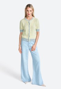 Knitted cardigan in pastel yellow with blue stripes, short sleeves, and button closure, paired with light blue wide-leg jeans.