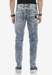 Hellblaue, ausgewaschene Slim-Fit-Jeans aus Denim mit zwei Gesäßtaschen, kontrastierenden Nähten und dekorativen Patches.