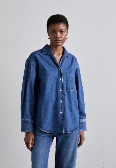 Cămașă din denim cu guler, mâneci lungi, buzunar frontal și închidere cu nasturi. Culoare albastră cu detalii vizibile de cusătură.