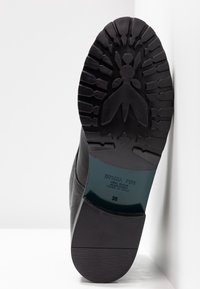 Semelle d'une botte en cuir noir montrant une empreinte avec un motif d'insecte, le nom de la marque Patrizia Pepe, la taille 39 et l'étiquette Made in Italy.