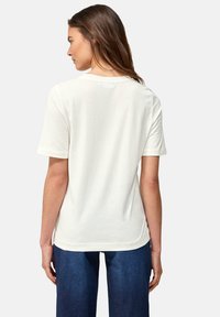 Camiseta de algodón blanca con manga corta, dobladillo ligeramente curvado y un corte relajado. La vista trasera muestra un diseño simple sin adornos.