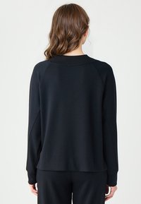 Czarna bluza z okrągłym dekoltem, raglanowymi rękawami i luźnym krojem. Tkanina wydaje się gładka z delikatnym połyskiem. Brak widocznych wzorów.