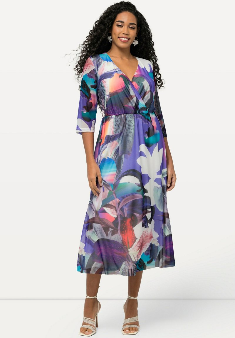 Lila Maxikleid mit einem lebhaften Blumenmuster, V-Ausschnitt, Dreiviertelärmel und elastischem Bund, kombiniert mit Riemchensandalen.