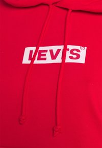 Sudadera roja de algodón con cordones blancos. Presenta un parche rectangular blanco que muestra el logo "LEVI'S®" en letras rojas en negrita.