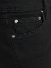 Gros plan sur la poche avant d'un jean en denim noir avec des coutures visibles et des rivets métalliques embossés avec « Jack & Jones ». 