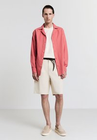 Kariert leinenshirt mit Knöpfen, weißes Rundhalshemd, beige Shorts, brauer Gürtel und hellbraune Slippers. Einfaches, lässiges Sommeroutfit.