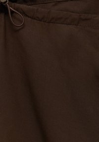 Bruine stof met een gladde textuur, met een tailleband met een trekkoord voor een verstelbare pasvorm. Geen herkenbare patronen of accenten zichtbaar.