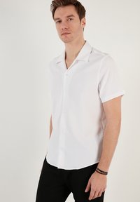Fehér, rövid ujjas ing, textúrált, bordázott mintával és hegyes gallérral, gombos elülső résszel és enyhén ívelt szegéllyel.