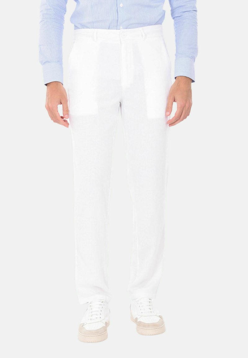 Pantaloni in lino bianchi con gamba dritta; presentano tasche frontali, passanti per cintura e chiusura con bottone. Abbinati a sneakers bianche e beige.