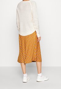 Pull en tricot de couleur crème avec un motif texturé, assorti à une jupe midi rayée jaune et orange et des baskets blanches.