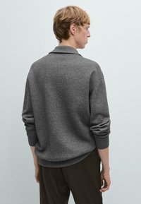 Maglione grigio con una vestibilità rilassata, caratterizzato da un collo a camicia e maniche lunghe. Realizzato in un materiale morbido e strutturato, con un orlo leggermente curvato.