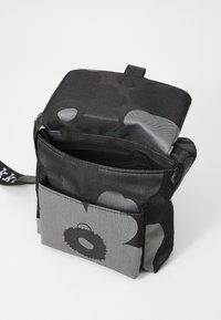 Black and gray fabric bag with floral pattern, open top, front zippered pocket, textured surface, and adjustable strap.