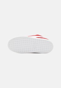 Baskets rouges avec semelle blanche, présentant une semelle extérieure en caoutchouc texturé et un design simple, affichant un style épuré et minimaliste.