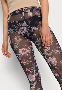 Leggings florais em malha preta transparente com padrões de flores multicoloridas. Apresentam um design ajustado e uma textura suave. Mão visível na perna.