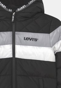 Zwarte pufferjas met diamantvormige gestikte textuur, met grijze en witte horizontale strepen, ritssluiting aan de voorkant en Levi's-logo op de borst.