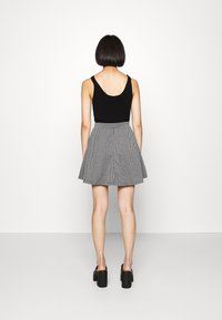 Musta toppi, jossa on syvä pyöreä selkäosa, yhdistettynä kellotettuun harmaa-valkoiseen haukanrautahameeseen. Malli pukeutunut massiivisiin mustiin korokepohjakenkiin.