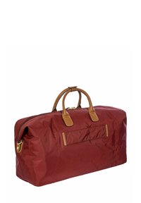 Sac de sport bordeaux avec des accents en cuir beige. Dispose de poignées arrondies, d'une fermeture éclair et d'une poche avant. Texture lisse et forme rectangulaire.