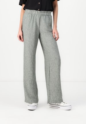 Hellgraue, weite Hosen mit einem elastischen Bund. Der Stoff hat ein strukturiertes, gewebtes Aussehen. Getragen mit weißen Sneakern.