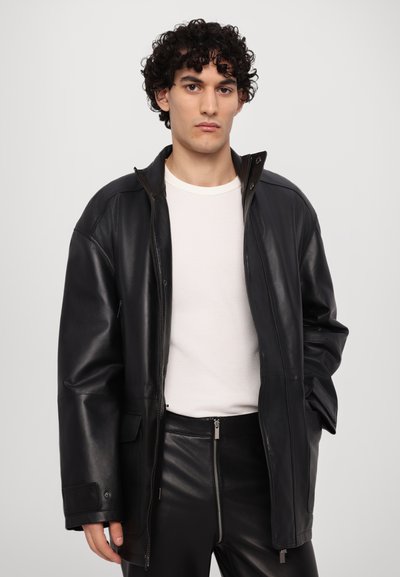 Cazadora de cuero negro con un alto cuello, diseñada con cierre de cremallera y bolsillos laterales. El material es suave y brillante, con un corte relajado.