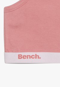 Rosa ermeløs topp laget av myk bomull, med en hvit ribb nederst med "Bench." trykt i rosa. Glatt tekstur, enkel design.