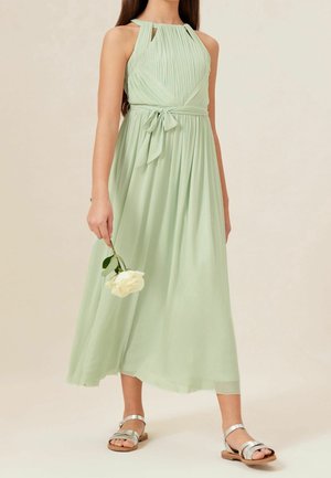 Hellgrünes, ärmelloses Kleid mit einem plissierten Oberteil, tailliert mit einer Schleife und einem fließenden Rock. Kombiniert mit silbernen Sandalen.