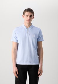 Polo shirt azzurro chiaro in morbido cotone, con una patta a tre bottoni e una piccola etichetta con logo sul lato sinistro del petto. Maniche corte.