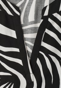 Tissu imprimé zèbre noir et blanc avec un col en V bordé d'un biais noir uni.