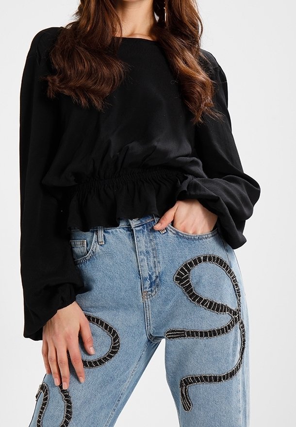 Top nero a maniche lunghe con vita arricciata, abbinato a jeans di jeans azzurri chiari con decorazioni a motivo di paillettes nere e argento.