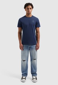 Navyblauwe katoenen T-shirt met ronde hals, gecombineerd met lichtblauwe distressed jeans met scheuren, en zwart-witte sneakers.