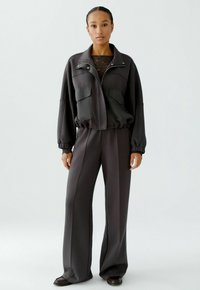 Grau tracksuit mit einer zipfelnden Jacke, die über zwei Fronttaschen verfügt, und weitem Hosen. Der Stoff wirkt glatt und hat einen lockeren Schnitt.