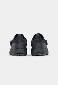 Black athletic shoes with a textured upper, reinforced heel, and a rubber sole. Features a round closure dial and branding on the sides.