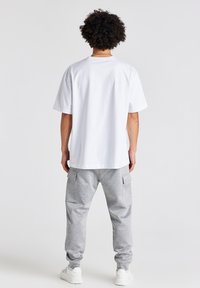 Hvid kortærmet t-shirt med rund hals, parret med grå sweatpants med sidelommer, sat mod en lys baggrund.