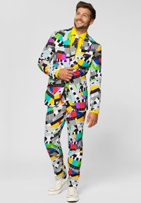 Colorful patterned suit with geometric shapes in yellow, green, pink, black, and white; paired with a bright yellow shirt and white sneakers.