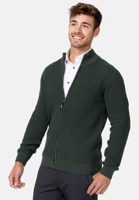 Sudadera de cremallera en verde oscuro con un diseño de tejido texturizado y puños y dobladillo de canalé. Presenta un cuello alzado y dos bolsillos con cremallera.