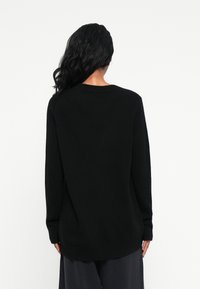 Sweater de malha preta com mangas longas, decote redondo e ajuste descontraído. Textura suave, comprimento médio com punhos e barra canelados.