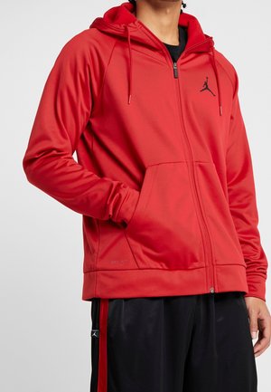 Felpa sportiva rossa con zip in tessuto liscio, dotata di cappuccio, tasche frontali e logo nero sul petto. Presenta polsini elastici e etichetta Dri-FIT.
