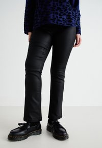 Zwarte nepleer broeken met een slim fit, met een gladde textuur en een lichte glans. Gecombineerd met zwarte schoenen en een gebreid trui met een patroon.