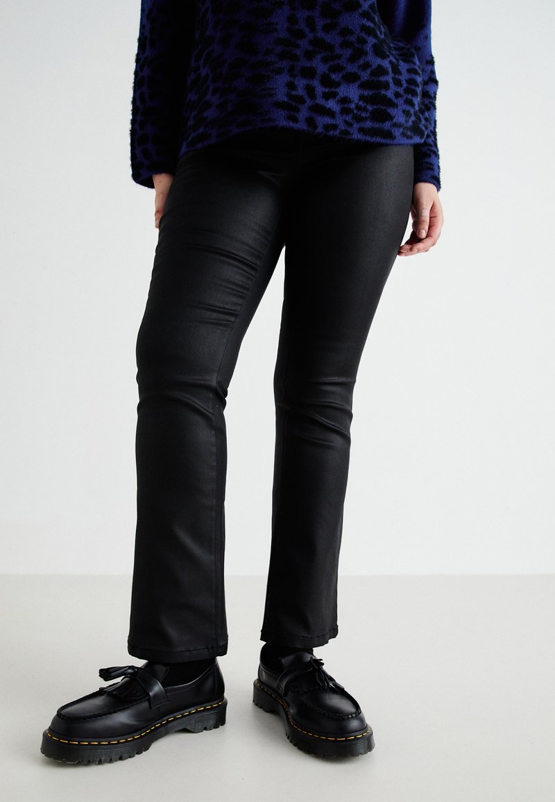 Zwarte nepleer broeken met een slim fit, met een gladde textuur en een lichte glans. Gecombineerd met zwarte schoenen en een gebreid trui met een patroon.
