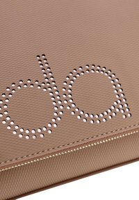 Bolso texturizado de color canela con un diseño perforado que forma la palabra "do" en detalles metálicos y una cremallera dorada en la base.