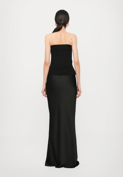 Top negro sin tirantes con diseño fruncido, combinado con una falda larga y lisa de color negro. El material parece suave y elegante, creando una silueta ceñida.