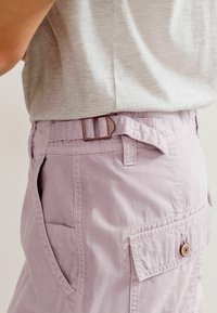 Shorts cargo violet clair avec poches latérales et poche arrière à rabat. Dotés d'une boucle de ceinture marron et d'une texture en coton doux.