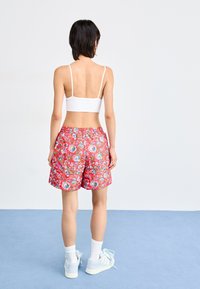 Piros virágmintás rövidnadrág elasztikus derékkal, fehér crop top-pal és világoskék sportcipővel párosítva.