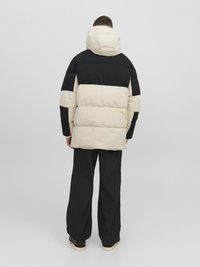 Pufferjack in crème en zwart, met een capuchon en horizontale strepen. Gecombineerd met zwarte wijde broek. Soepele textuur, robuust ontwerp.