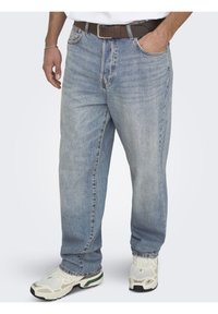 Jeans en denim bleu clair avec une coupe décontractée, dotés d'une jambe droite et de coutures visibles. Associés à une ceinture marron et des baskets blanches.