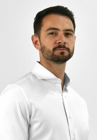 Witte blouse met lange mouwen en een puntige kraag, gladde textuur en knoopsluiting aan de voorkant. Model staat tegen een effen lichte achtergrond.