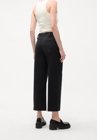 Sorte viddebukser med høj talje, baglommer og en glat tekstur. Bær dem med en tætsiddende cremefarvet tanktop og sorte platformsko.