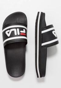 Chanclas negras de diapositiva con una correa ancha que presenta un logo de FILA en blanco y un acento rojo, suela de goma texturizada y rayas blancas a lo largo del costado.