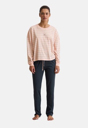 Helles rosa Langarmhemd mit horizontalen Streifen und einem kleinen Logo; kombiniert mit dunkelblauen, locker sitzenden Hosen mit einem elastischen Bund.