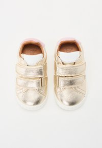 Złote metaliczne sneakersy z dwoma paskami na rzepy, różowymi akcentami na pięcie i gumową podeszwą. Gładka faktura z delikatnymi przeszyciami.